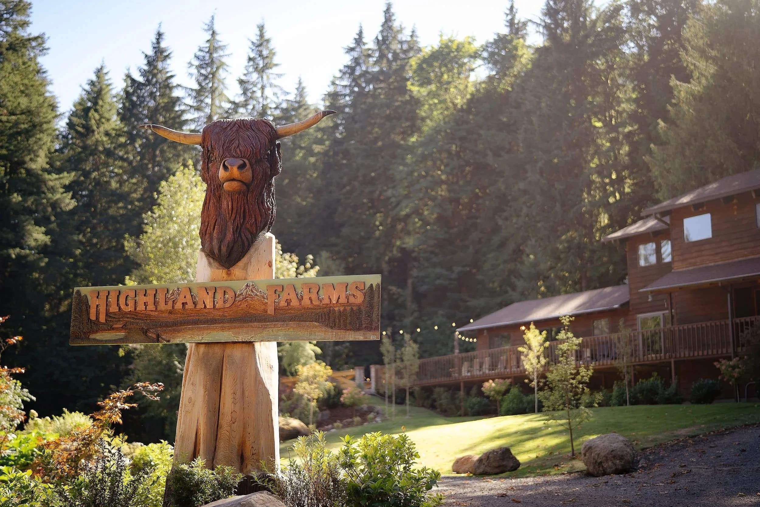The carved Highland cow on a post above a sign reading Highland Farms, the Lodge behind it in the trees