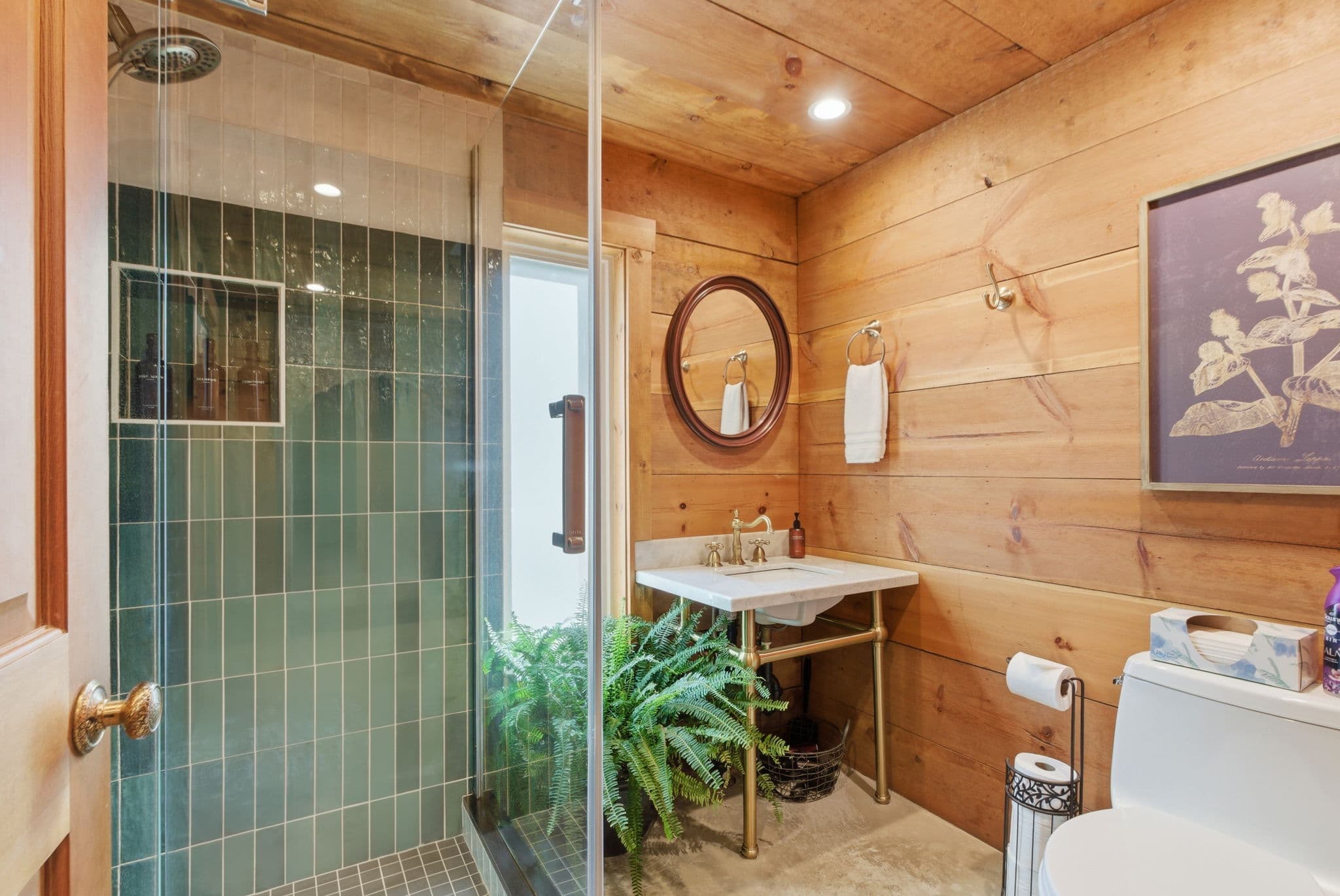 Cottage bathroom with green tile shower, brass fixtures, and pine walls
