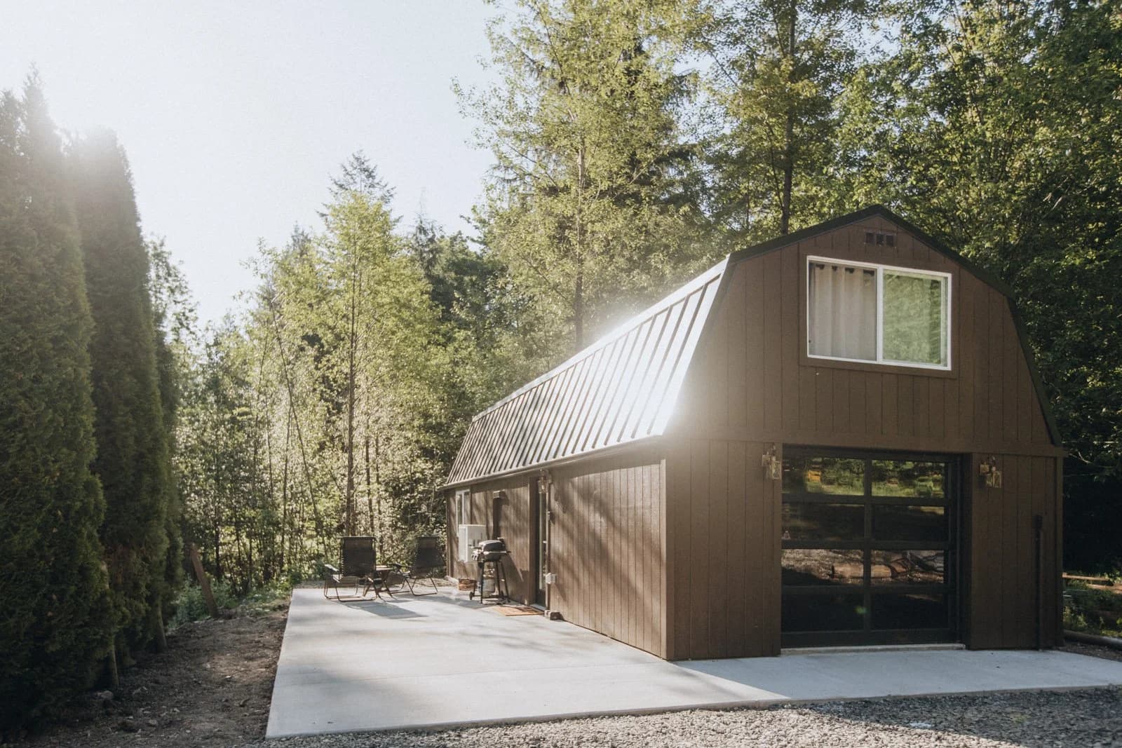 Bonnie Lass Cottage, a cedar cabin with a barn-style roof, backlit among tall firs