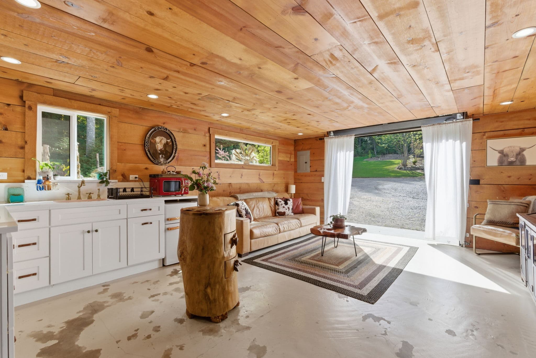 Living room with garage door open to forest, leather sofa, and tree-trunk side table