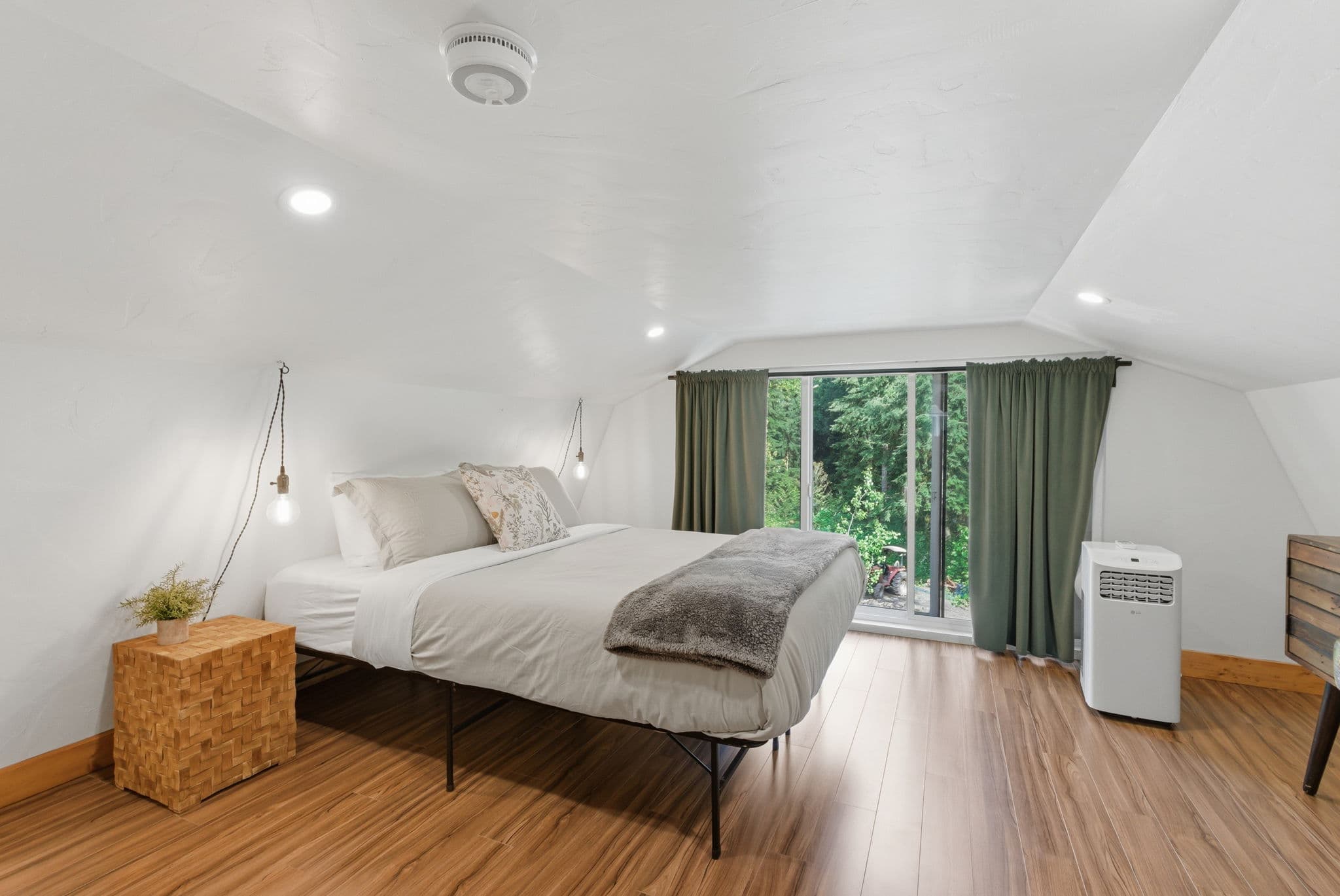 Loft bedroom with sloped white ceiling and green-curtained dormer window
