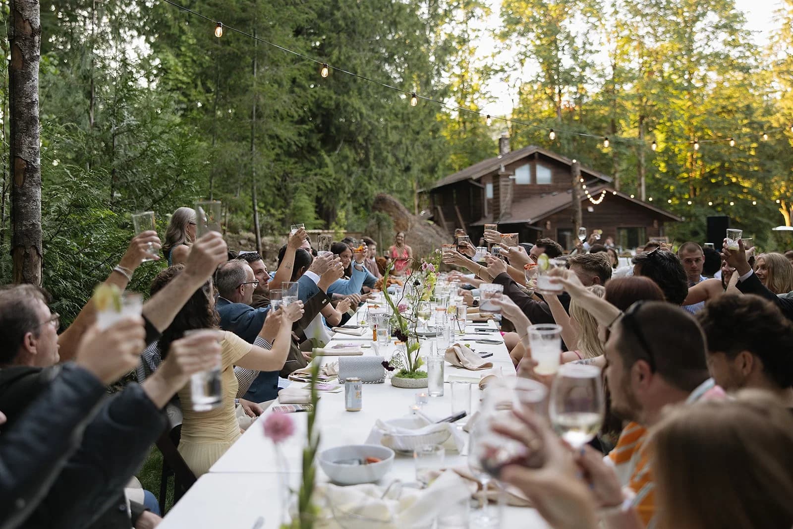 Guests raise their glasses along one long table under the trees, with the Lodge behind