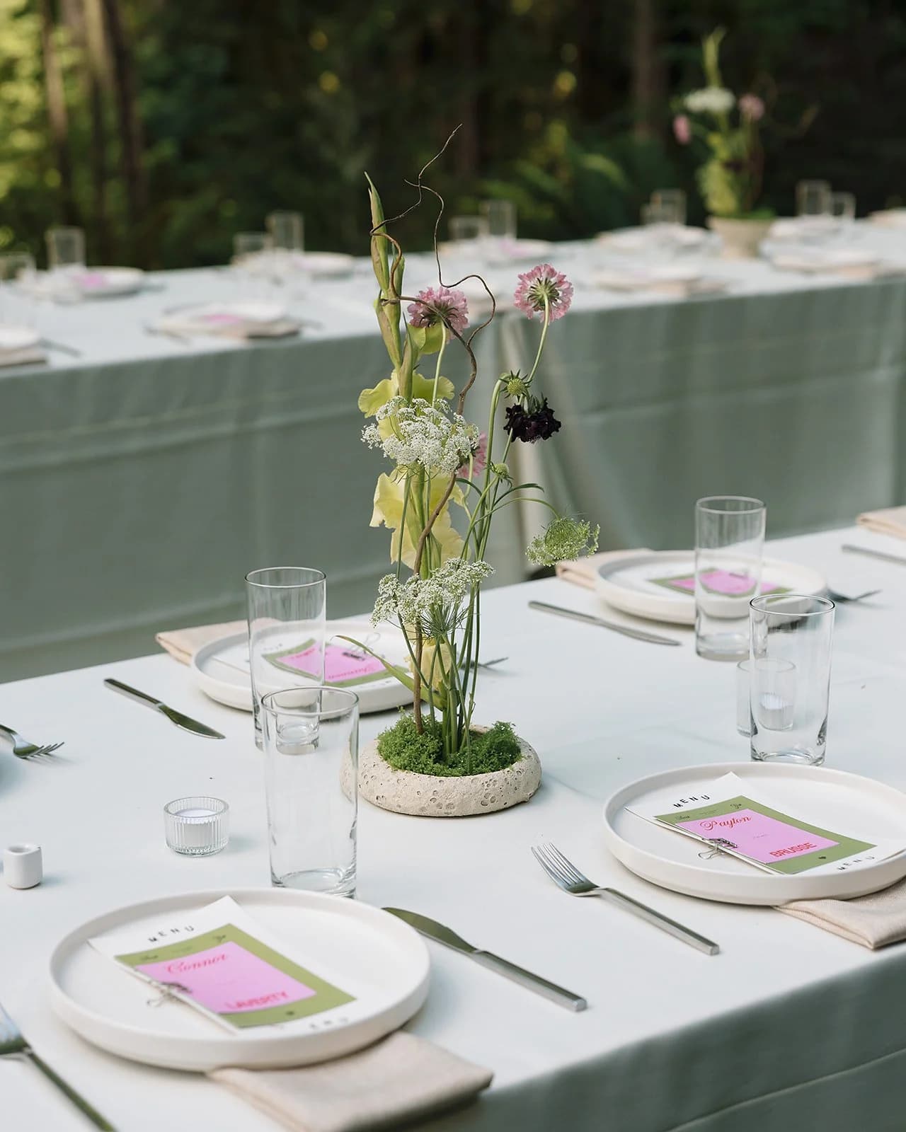 A long table set with sage linens, pink menu cards and wildflowers