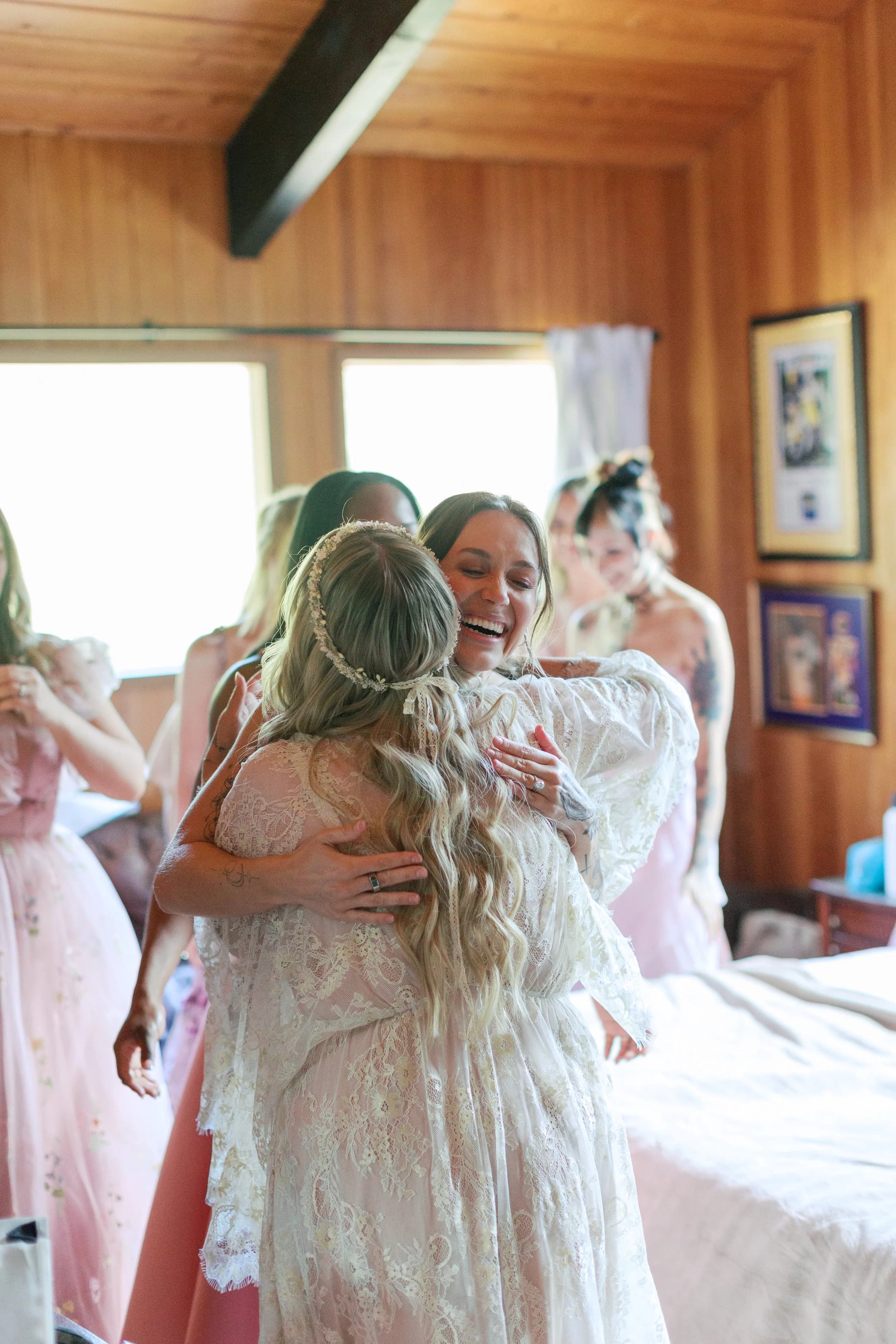 A bride hugs her bridesmaids in a cedar-walled bedroom